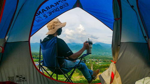 Side view of man sitting in tent against sky