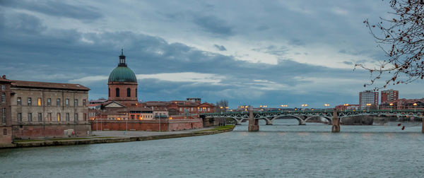 Bridge over river amidst buildings in city against sky