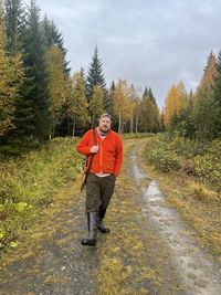 Rear view of a man walking in the woods with a rifle during hunting season on an autumn day.