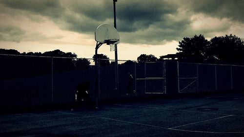 Silhouette of bicycle parked by fence against cloudy sky