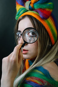 Close-up portrait of young female model holding magnifying glass against black background