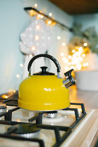 A yellow teapot stands on the stove in the kitchen against the background of christmas lights