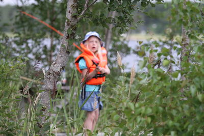 Girl with fishing rod standing by tree