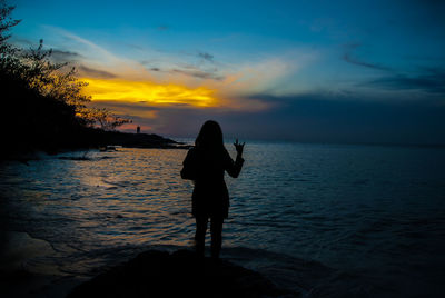 Silhouette man standing on beach against sky during sunset