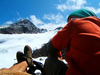 Low section of people sitting on snowcapped mountain against sky