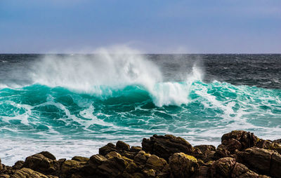 Waves breaking against rocks in sea against clear sky