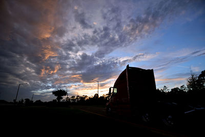 Road by silhouette city against sky during sunset