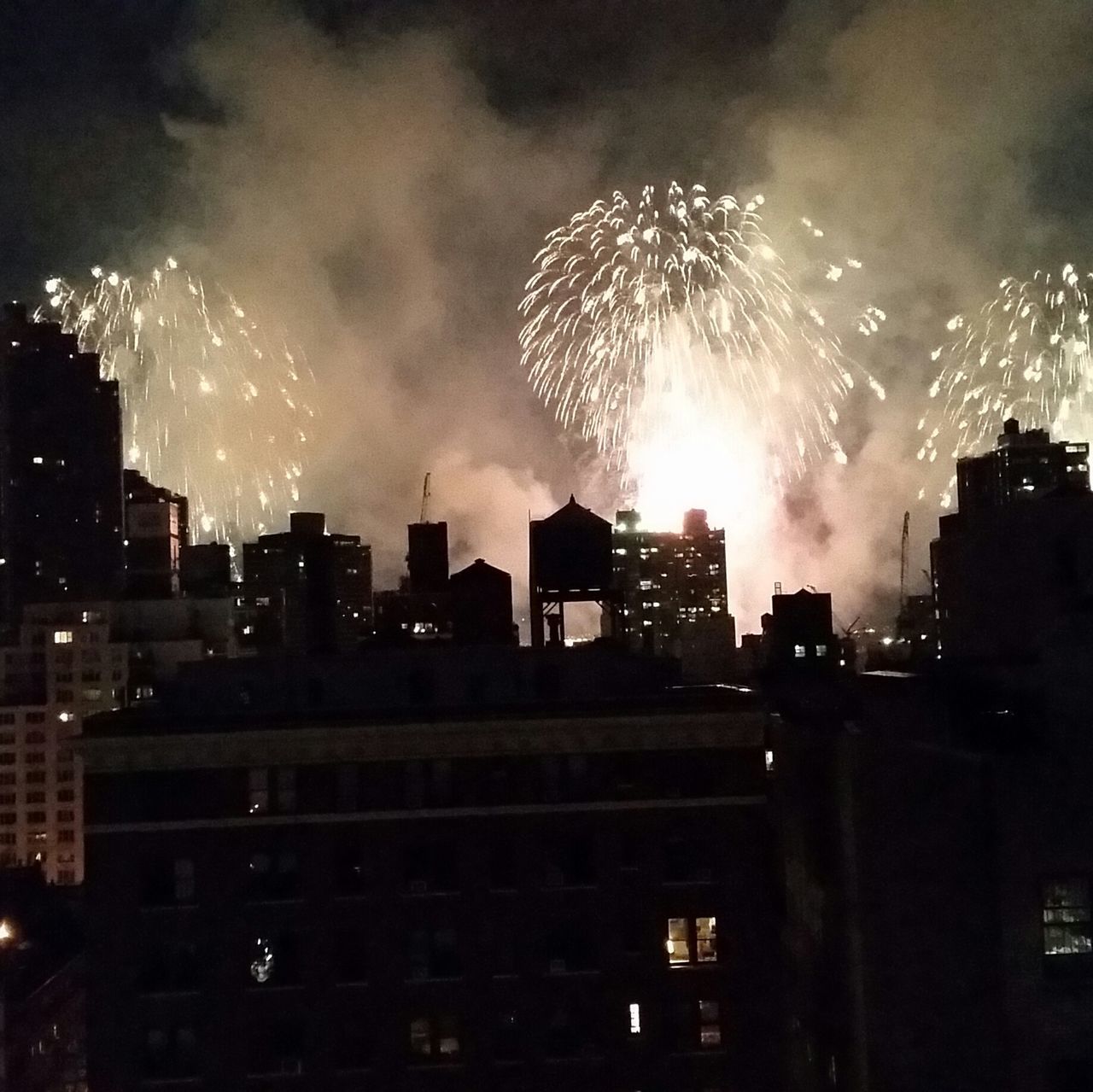 illuminated, night, building exterior, architecture, built structure, city, firework display, exploding, sky, long exposure, cityscape, glowing, skyscraper, firework - man made object, celebration, firework, smoke - physical structure, city life, light - natural phenomenon, sparks