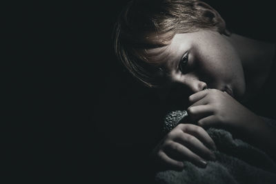 Close-up portrait of girl with thumb in mouth against black background