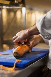 Cropped image of chef peeling vegetable in kitchen