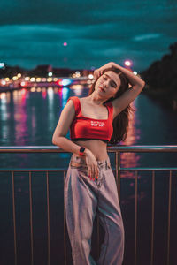 Smiling young woman standing on bridge over river at night