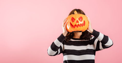 Rear view of woman holding pumpkin against yellow background