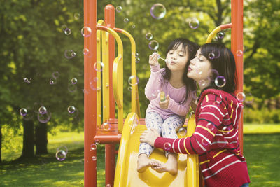 Mother and daughter blowing bubbles at slide in park