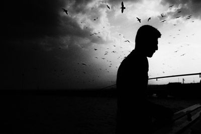 Silhouette man standing by sea against sky during sunset