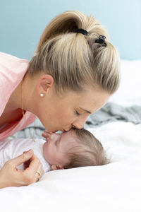 Mother kissing baby girl on bed at home