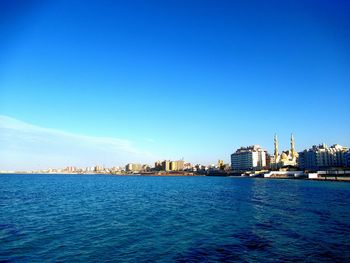 Sea and buildings against clear blue sky