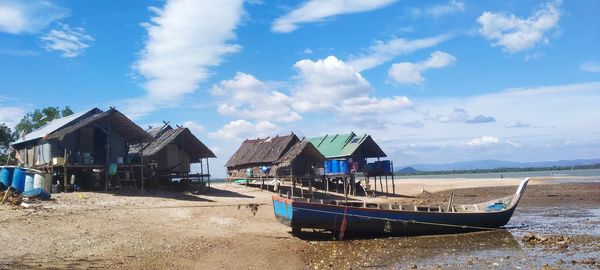 Boats moored on beach by buildings against sky