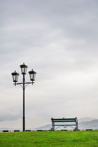 Street light on bench on field against sky