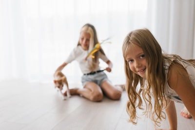 Caucasian girls sisters play with the cat cornish rex at home on a sunny day, hugs him and laughs