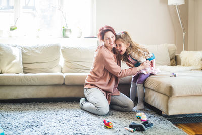 Smiling woman embracing daughter sitting on sofa at home