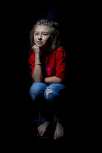 Portrait of girl sitting against black background
