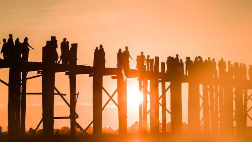 Silhouette people standing by railing against sky during sunset