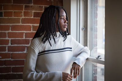 Thoughtful young woman looking through window at home