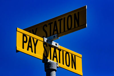 Low angle view of road sign against clear blue sky