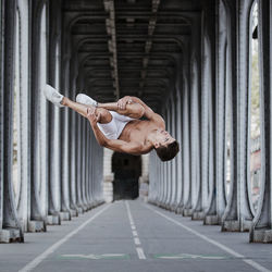Shirtless man jumping below bridge in city
