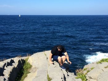 People sitting on rock looking at sea against sky