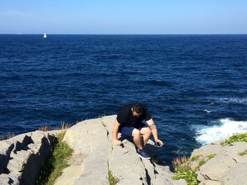 High angle view of man sitting on cliff with sea in background 