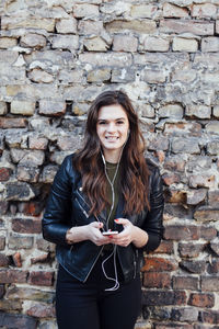 Portrait of smiling young woman standing against brick wall