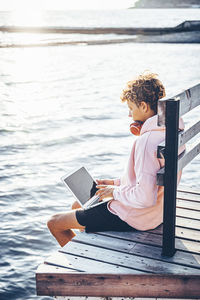 Man using laptop while sitting on pier