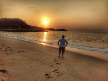 Rear view of woman on beach against sky during sunset