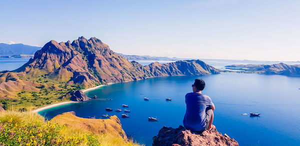 Rear view of man looking at lake by mountain against sky