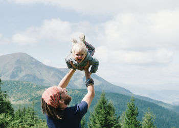 Father lifting daughter on mountain against sky