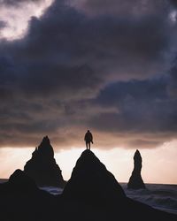 Silhouette man standing on rock at beach against sky during sunset