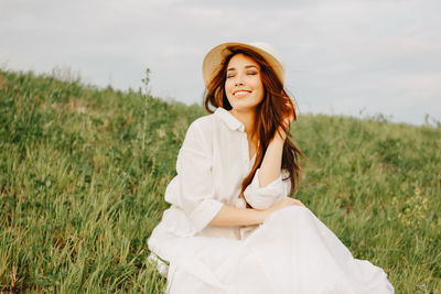 Woman sitting on grass against sky