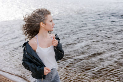 Young stylish woman in light light t-shirt and leather jacket and curly hair