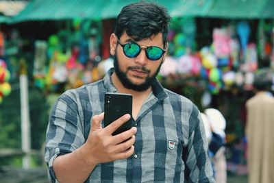 Young man wearing sunglasses using mobile phone while standing in market