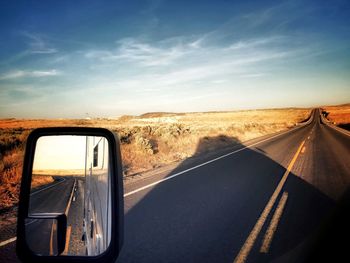 Vehicle reflecting in side-view mirror on road against sky