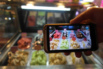 Cropped hand of person photographing colorful ice creams in container on smart phone