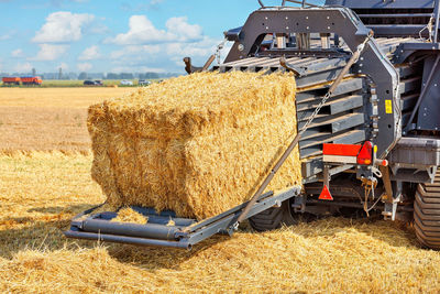 A fragment of an agricultural tractor forming bales of straw against the background of a field.