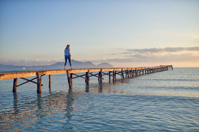 Woman walking on pier in sea against clear sky