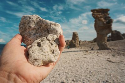 Close-up of person holding rock against sky