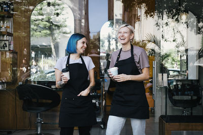 Cheerful female coworkers with coffee cup standing against hair salon