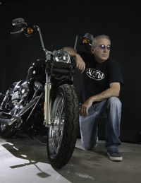 Full length of man kneeling by motorcycle against black background