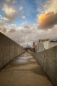 View of footpath in city against cloudy sky