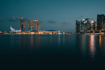 Illuminated city by sea against sky at night