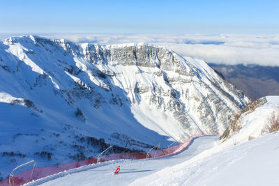 A ski trail with an orange fence grid against a backdrop of snowy cliffs and low-hanging clouds